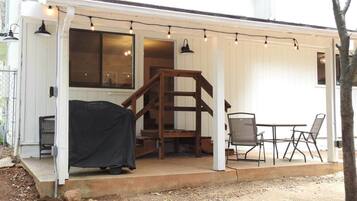 A covered outdoor area with a grill, a staircase, and a table with chairs.