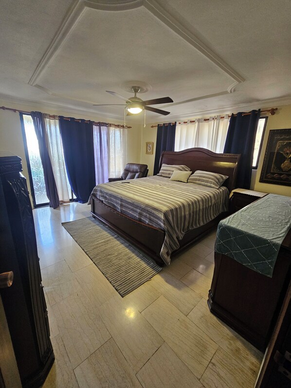 A bedroom with a bed, a chair, a desk, a ceiling fan, and a window with curtains.