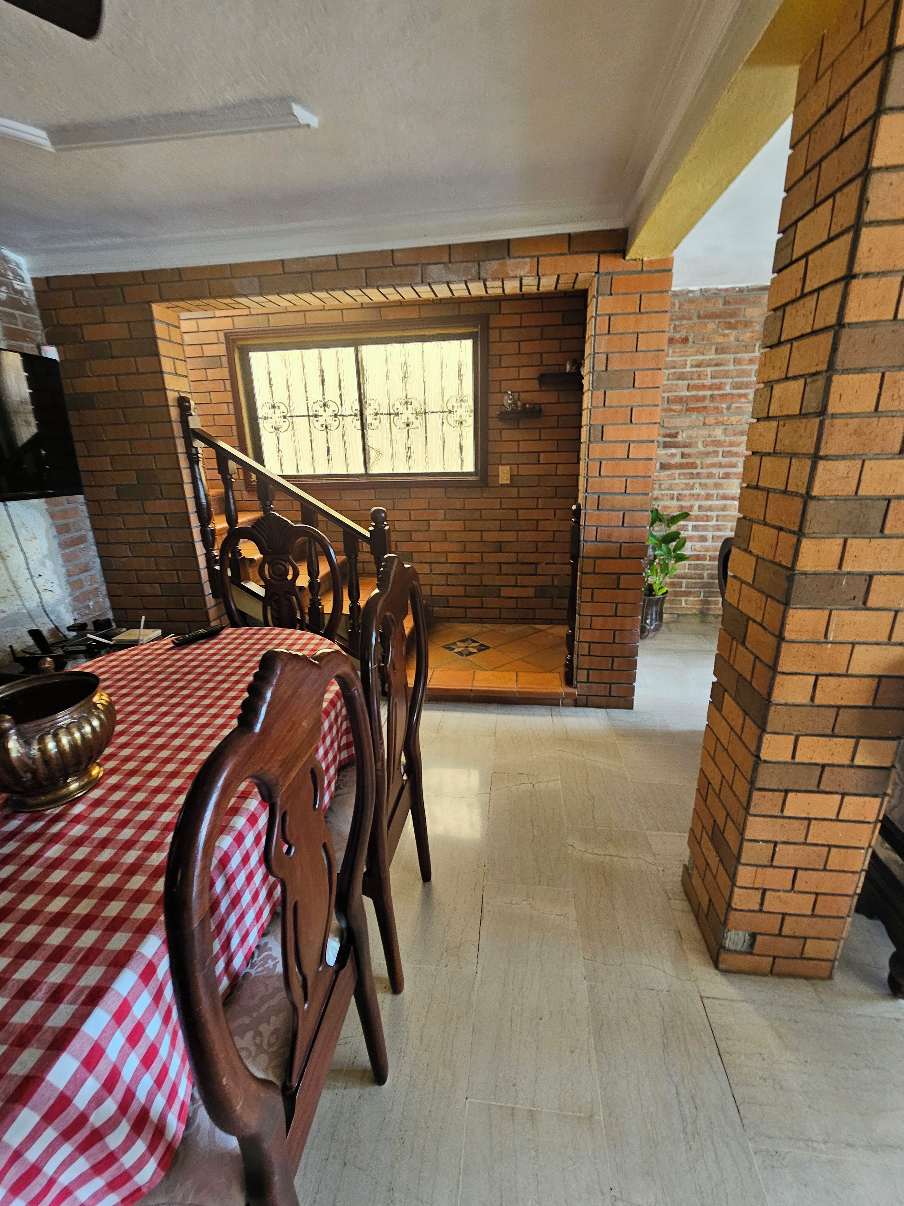 A dining area with a checkered tablecloth, wooden chairs, and a brick wall.