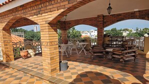Eine überdachte Terrasse im Freien mit Backsteinbögen, Terrakottafliesen und Gartenmöbeln.