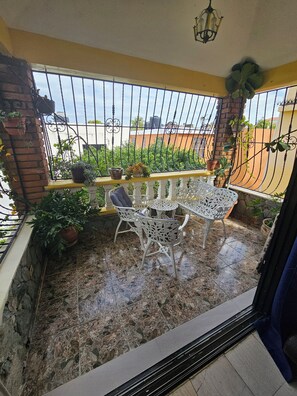 Un balcon avec un sol carrelé, une table et des chaises en métal blanc, des plantes en pot et une vue sur le quartier.