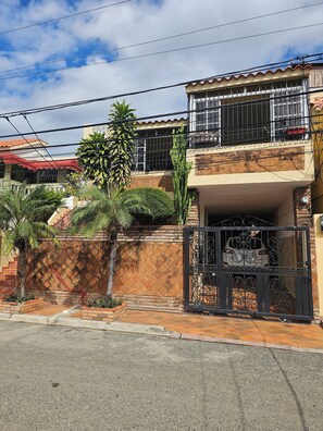 Un edifici residencial amb entrada tancada per reixa, un balcó amb barana metàl·lica i una escala que condueix a l'entrada.