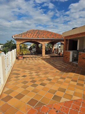 A rooftop patio with a tiled floor, a brick pergola, and potted plants.