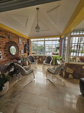 A room with wicker chairs, a brick wall, and a large window with a view.