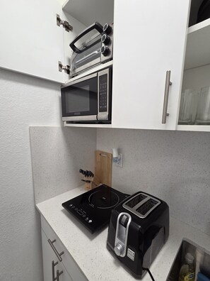Una kitchenette compacta equipada con microondas, tostadora y placa de inducción.