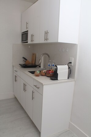 Een kleine keuken met witte kasten, een magnetron, een broodrooster en een spoelbak.