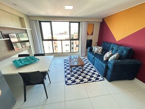 Ein modernes Wohnzimmer mit einer Couch, einem Couchtisch, einem Esstisch und einem großen Fenster.