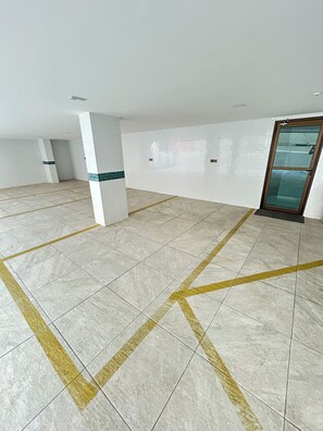 A spacious indoor area with tiled flooring and a glass door. - Melhores Flats - Divino, pertinho do mar (João Pessoa)