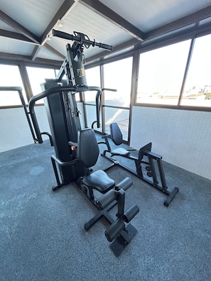 Une salle de sport équipée de matériel d’exercice, dotée de grandes fenêtres et offrant une vue sur la ville.