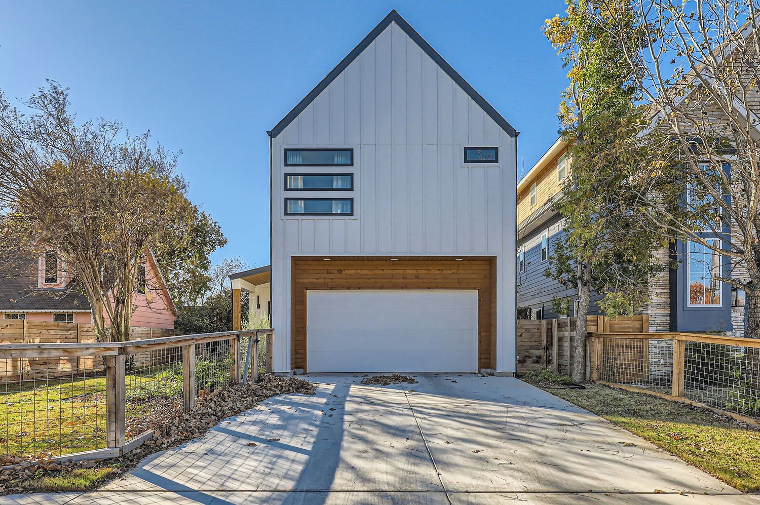 A modern two-story house with a garage, surrounded by a wooden fence and trees.