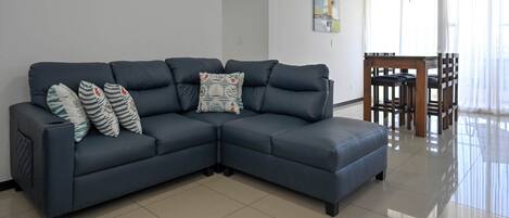 A modern living room with a dark blue sectional sofa, a dining table with chairs, and a ceiling fan.