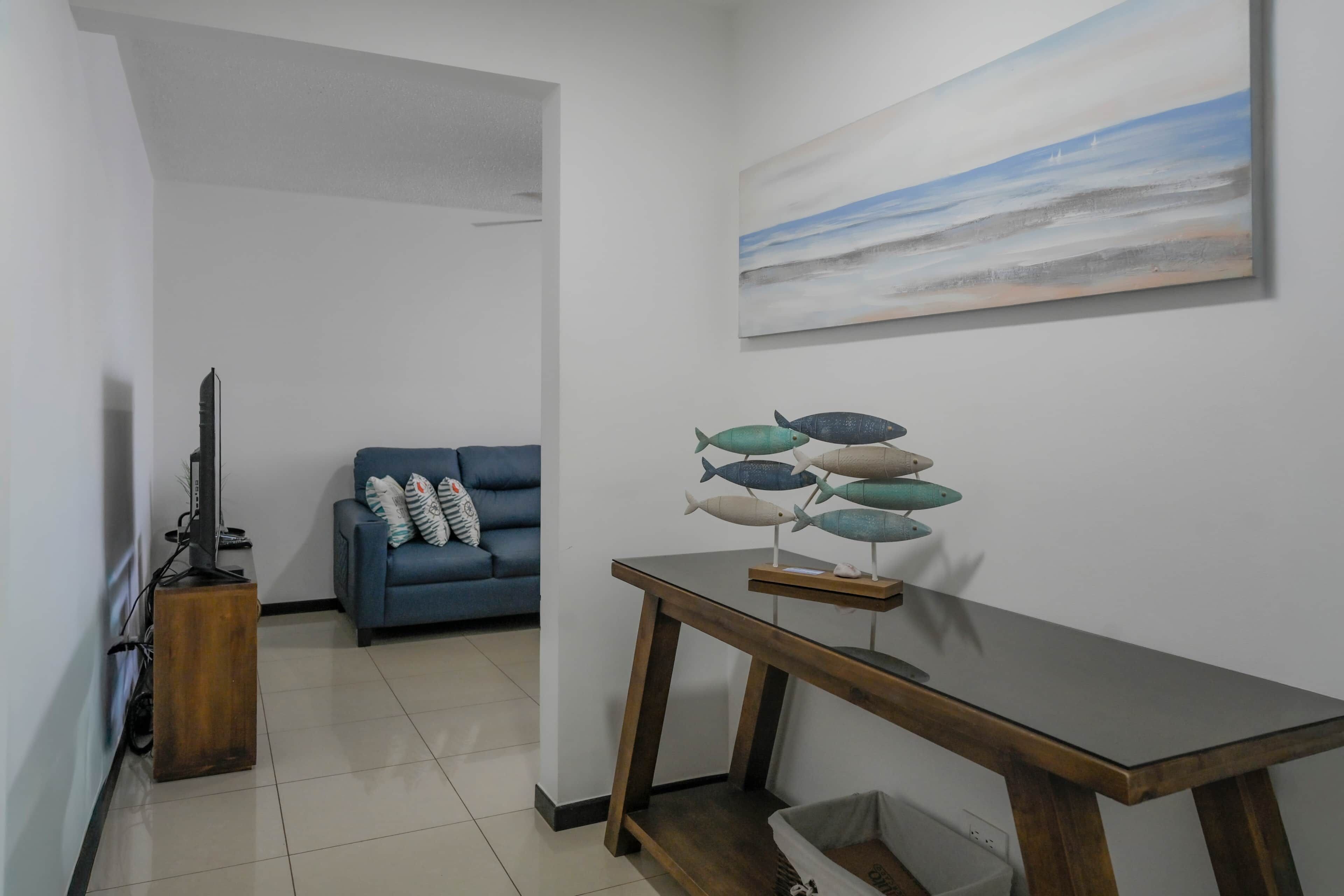 Una sala de estar con un sofá azul, una mesa de centro de madera y un cuadro de un paisaje marino.
