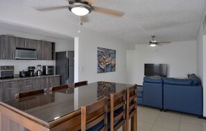 A modern kitchen with a dining area, a living room with a sofa and TV, and a ceiling fan. - Costa Linda Modern Apto·Walk to the beach·Pool/AC (Punta Arenas)