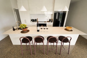 A modern kitchen with a central island, bar stools, a refrigerator, and pendant lighting. - Nature Retreat | Entire 3BR Home | Sleeps up to 7 (McLaren Vale)