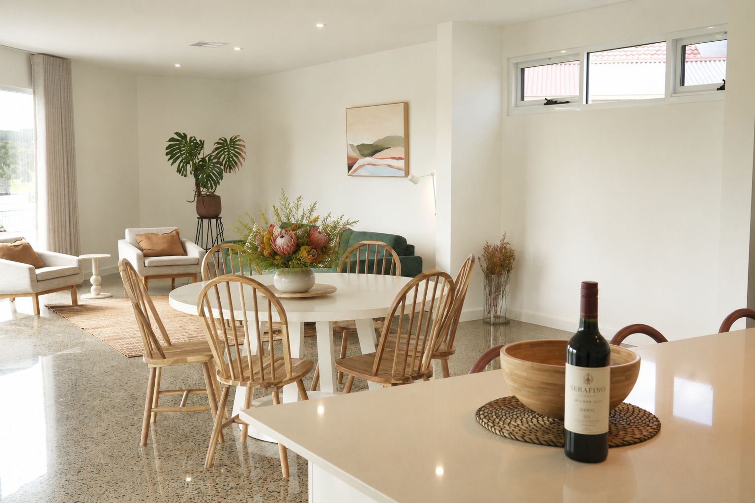 A modern dining area with a round table, wooden chairs, and a bottle of wine on a placemat.