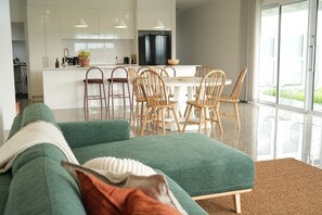 Ein modernes Wohnzimmer mit einem grünen Sofa, Holzstühlen, einem Esstisch und einer Küche im Hintergrund.