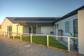 Ein modernes Haus mit einer Solaranlage auf dem Dach, einem eingezäunten Garten und einem Schotterweg.