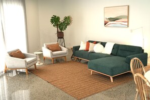 A modern living room with a green sofa, a white armchair, and a coffee table. There is a potted plant and a painting on the wall. - Nature Retreat | Entire 3BR Home | Sleeps up to 7 (McLaren Vale)