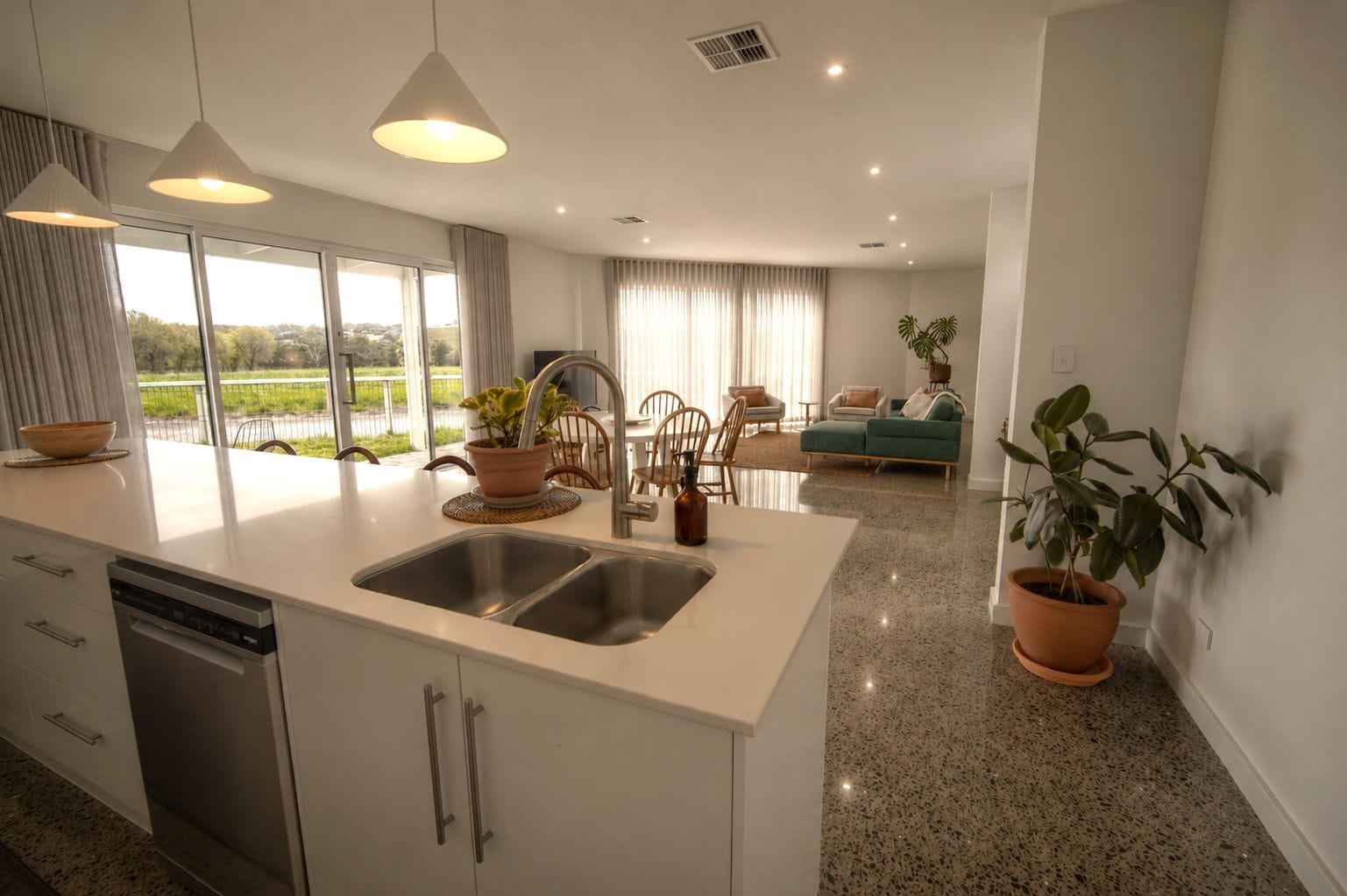 A modern kitchen with a large island, stainless steel appliances, and a dining area with a green sofa and chairs.