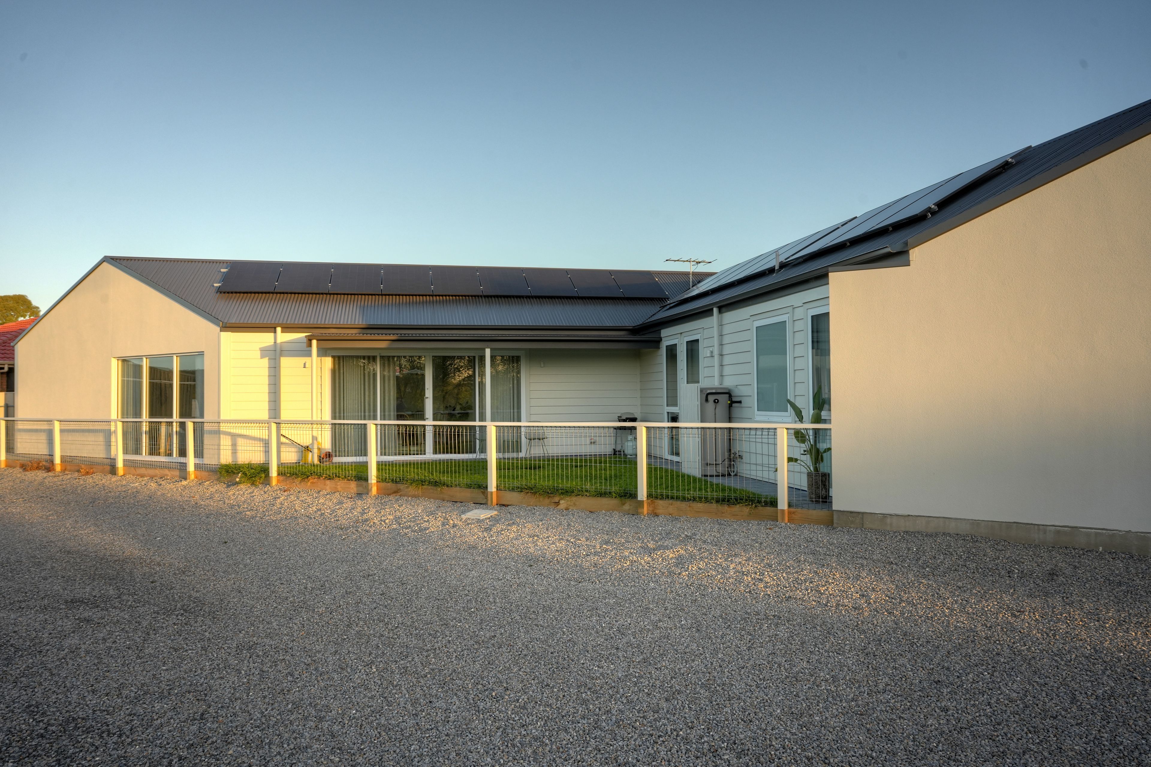 A modern building with a sloped roof, large windows, and a gravel driveway.