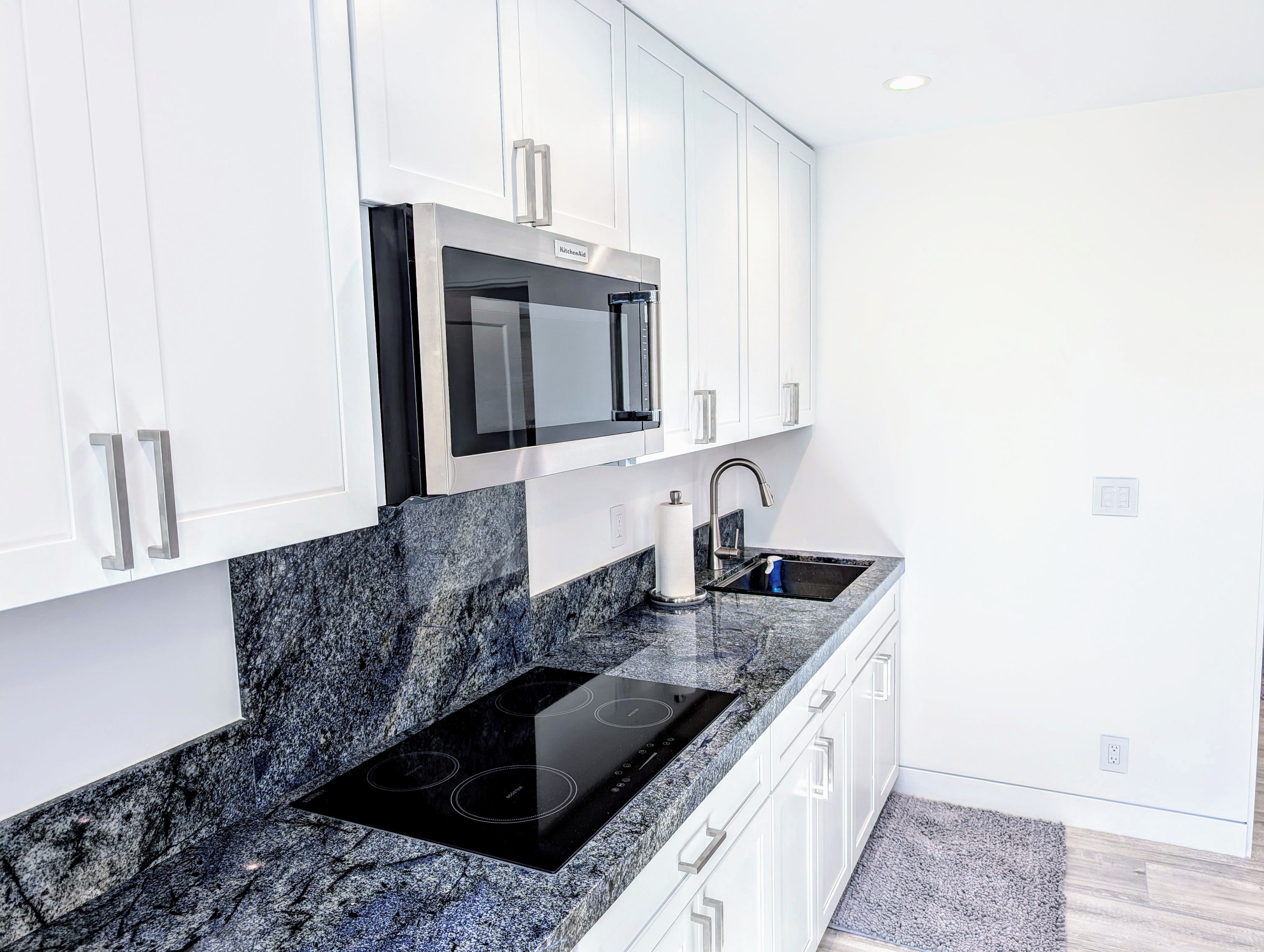 A modern kitchen with white cabinets, a black microwave, a stainless steel sink, and a black induction cooktop.