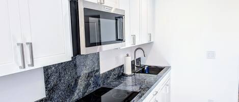 A modern kitchen with white cabinets, a black microwave, a stainless steel sink, and a black induction cooktop.
