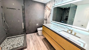A modern bathroom with a glass-enclosed shower, a large mirror, and a vanity with a marble countertop. - Beach Front - Studio Condo, Luxury Finishes, Walk to Everything, 440 sq ft, WIFI (Huntington Beach)