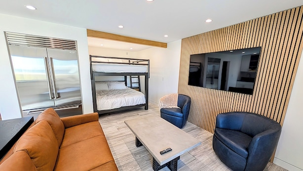 A modern room with a bunk bed, a sofa, a coffee table, and a TV mounted on a wooden panel wall. - Beach Front - Studio Condo, Luxury Finishes, Walk to Everything, 440 sq ft, WIFI (Huntington Beach)