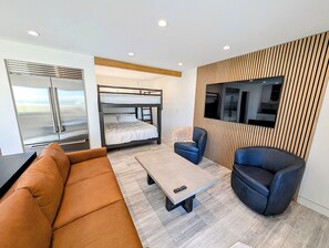 Une chambre moderne équipée d’un lit superposé, d’un canapé, d’une table basse et d’un téléviseur fixé sur un mur recouvert de panneaux en bois.