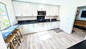 A modern kitchen with white cabinets, a granite countertop, and a built-in microwave. - Beach Front - Studio Condo, Luxury Finishes, Walk to Everything, 440 sq ft, WIFI (Huntington Beach)