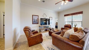 A living room with a leather sofa, a leather armchair, a flat-screen TV, and a wooden coffee table. - Wrangler Hideaway - 3.6 miles to Kyle Field (College Station)