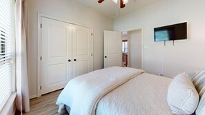A bedroom with a bed, a television mounted on the wall, and a door leading to another room. - Wrangler Hideaway - 3.6 miles to Kyle Field (College Station)