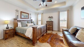 A bedroom with a wooden bed, a leather sofa, a cowhide rug, a dresser, and a ceiling fan. - Wrangler Hideaway - 3.6 miles to Kyle Field (College Station)