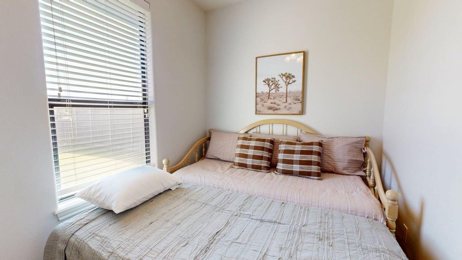 Een slaapkamer met een bed, een raam met zonwering en een aan de muur hangend schilderij.