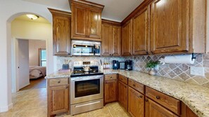 A kitchen with wooden cabinets, stainless steel appliances, and a granite countertop. - Wrangler Hideaway - 3.6 miles to Kyle Field (College Station)