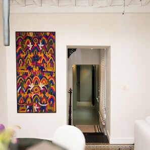 Un pasillo con un cuadro abstracto de colores en la pared, una escalera que lleva a otra habitación y una puerta blanca al final.