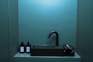 Ein Badezimmer mit einem schwarzen Waschbecken, zwei Lotionflaschen und einem schwarzen Wäschekorb für Handtücher.