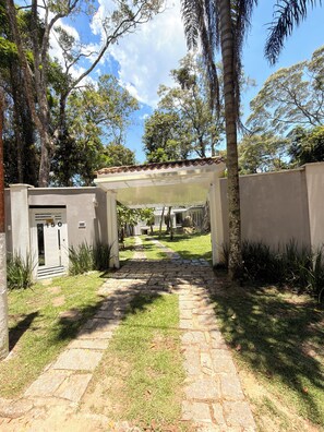 A pathway leading to a building with a covered entrance, surrounded by greenery and trees.