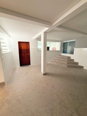 A spacious interior with a staircase leading to an upper level, white tiled walls, and a wooden door. - Country house with heated pool in the heart of Cantareira, 30 minutes from São Paulo. (Caieiras)