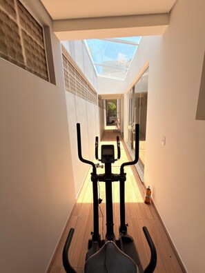 A narrow hallway with a ceiling skylight, leading to a patio area with exercise equipment.