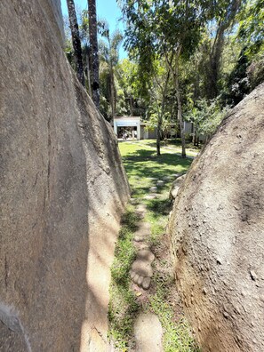 A pathway leading to a building surrounded by large rocks and trees. - Country house with heated pool in the heart of Cantareira, 30 minutes from São Paulo. (Caieiras)