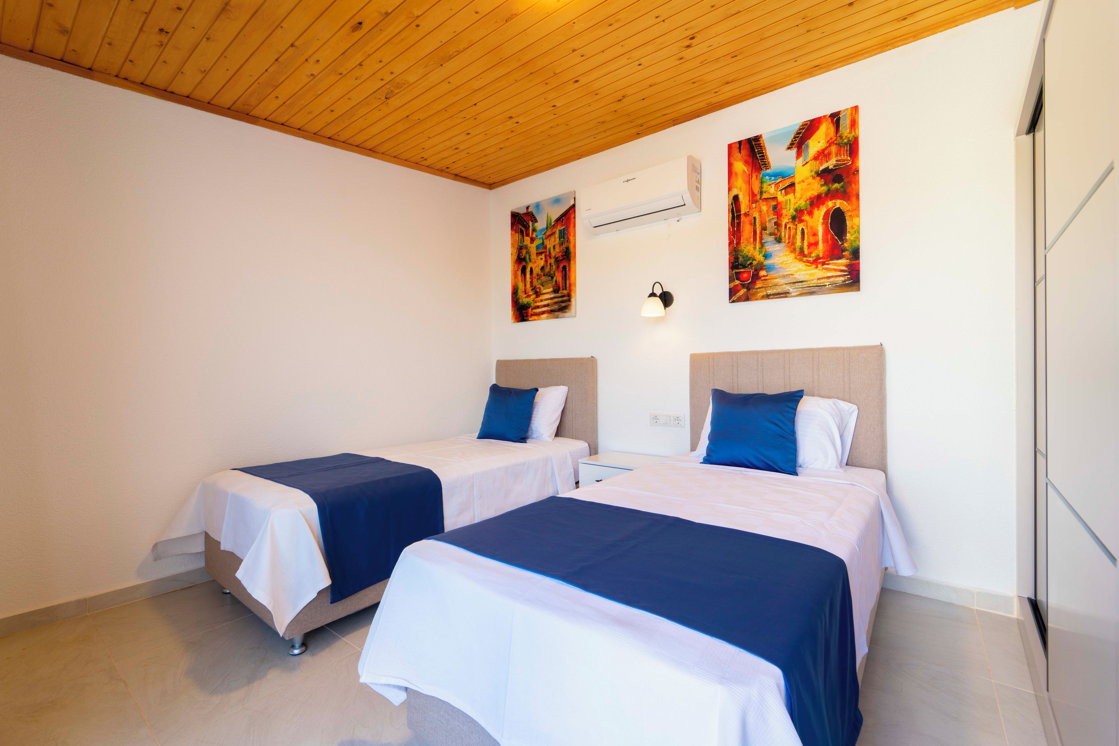 Una habitación de hotel con dos camas, techo de madera y dos cuadros en la pared.