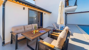Un área de estar al aire libre con mesa de madera, sillas acolchadas y vista a la piscina.