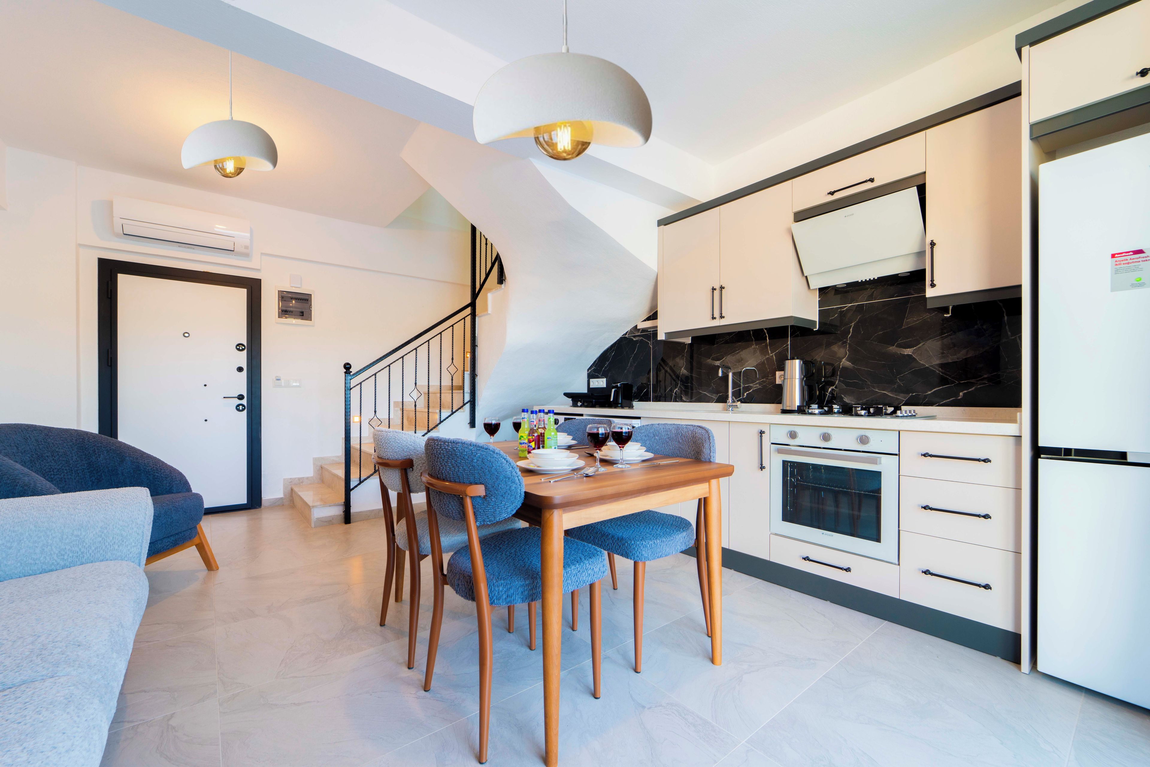A modern kitchen with a dining area, a staircase, and a living room with a sofa.