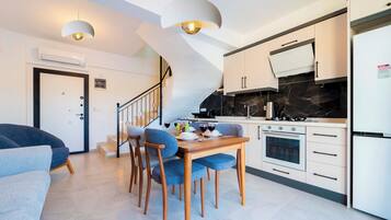 A modern kitchen with a dining area, a staircase, and a living room with a sofa.