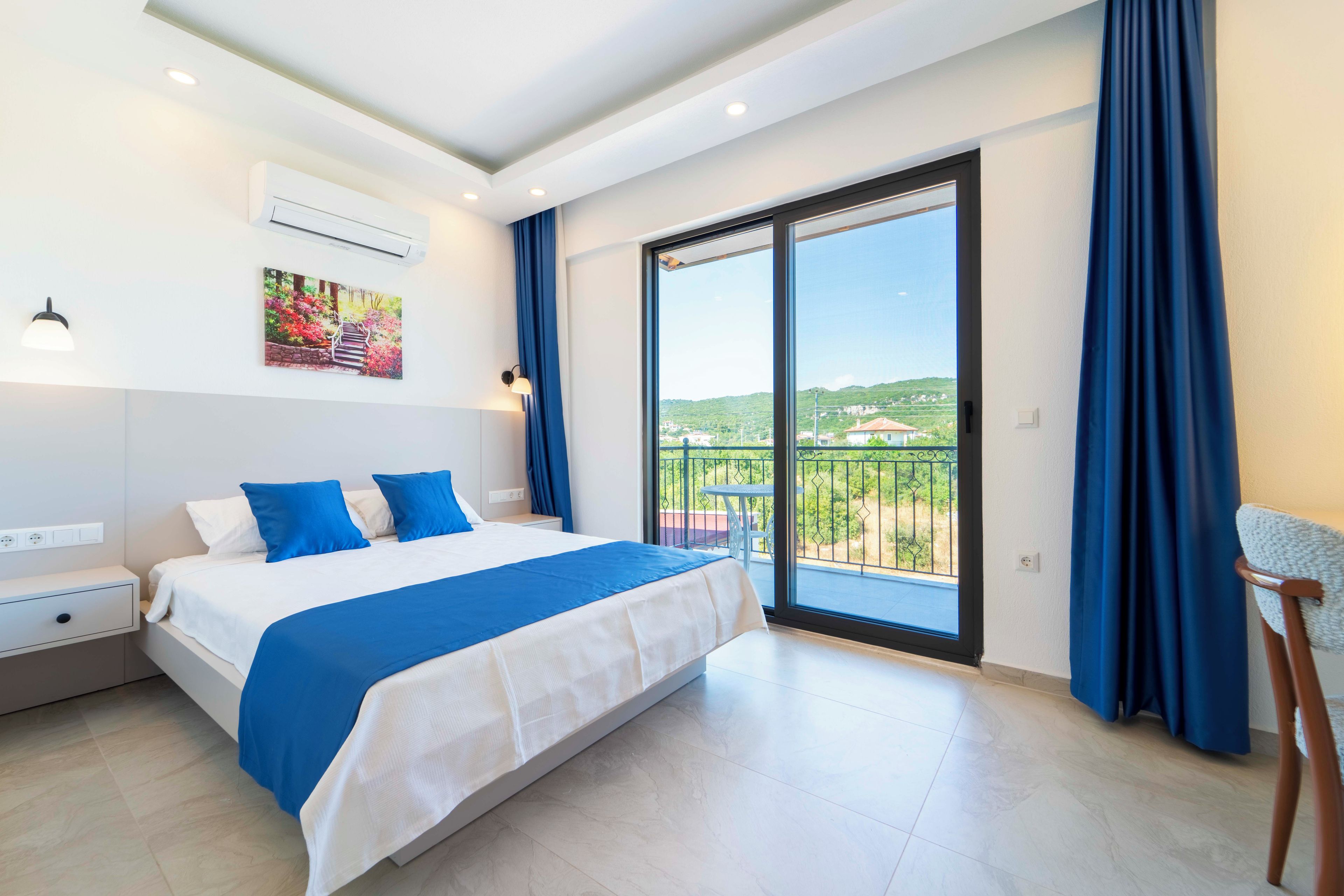 Ein Hotelzimmer mit Bett, Nachttisch, Schreibtisch, Stuhl, einem Balkon mit Aussicht und einer Klimaanlage.