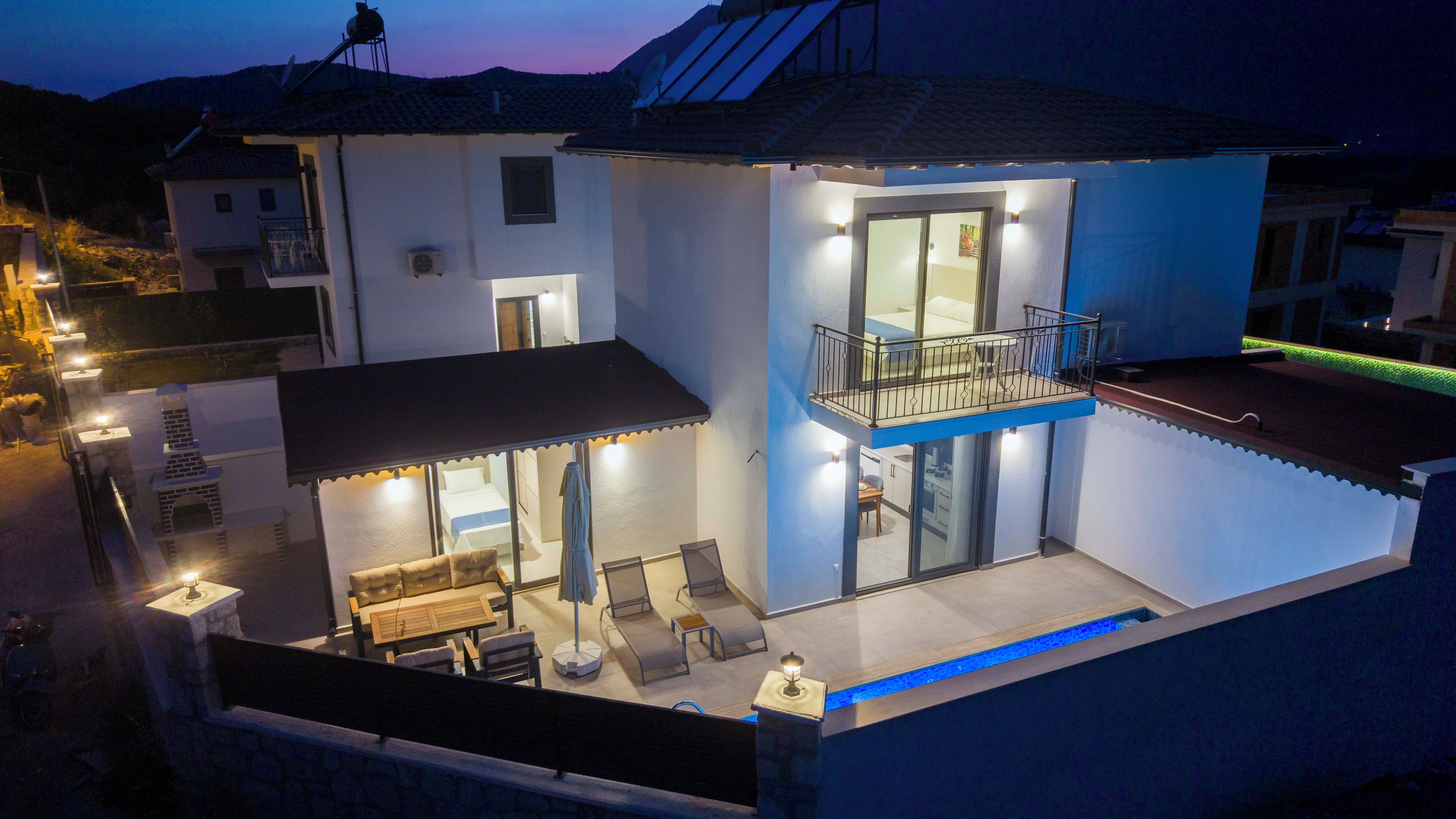 A two-story house with a balcony, a patio with seating, and a swimming pool.