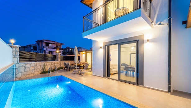 Una casa moderna de dos pisos con piscina, mobiliario exterior y un balcón.