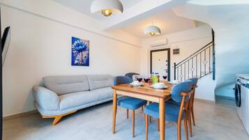 A modern living room with a sofa, dining table, chairs, and a painting on the wall.