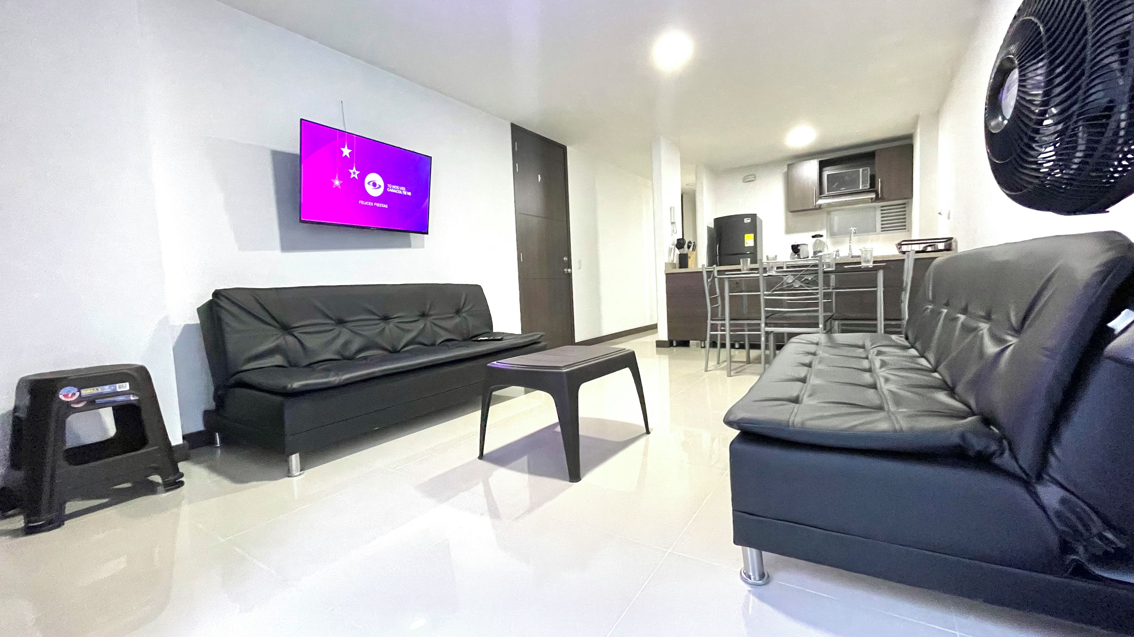 Una sala de estar moderna con un sofá negro, una mesita y un televisor de pantalla plana montado en la pared.